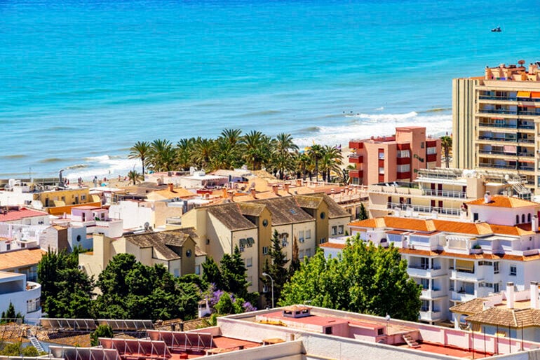 View of a bright blue sea and brightly colored resort-style city buildings in Torremolinos, Spain in the Costa del Sol