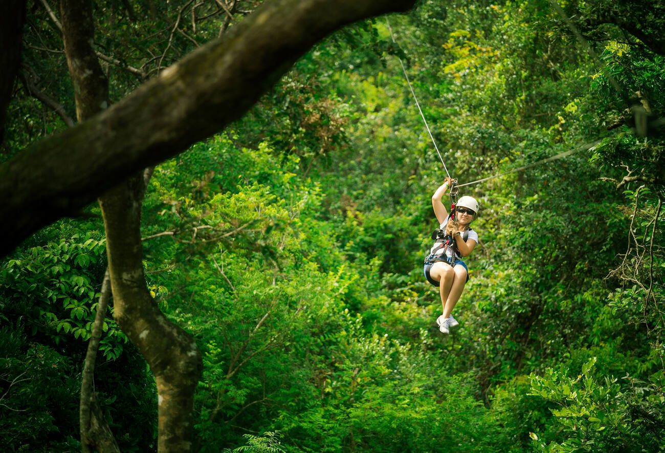 A woman in her 40s riding a zipline between trees.