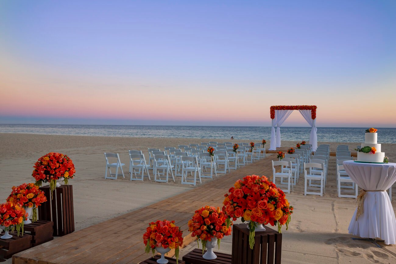 Beach wedding alter and seating set up with a wooden aisle and orange flower accents