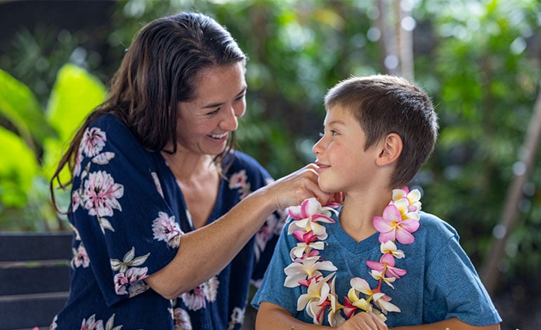 A staff member of the OUTRIGGER Kona Resort & Spa places a lei around a boy's neck