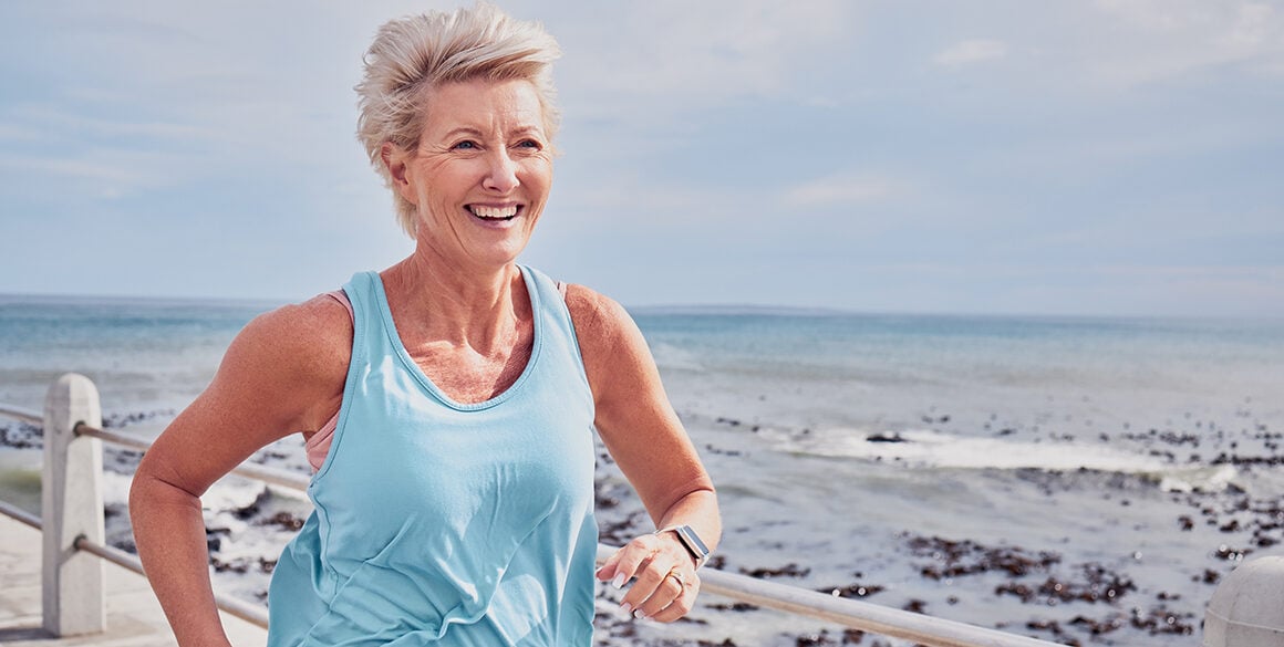 A senior woman running along a boardwalk, smiling