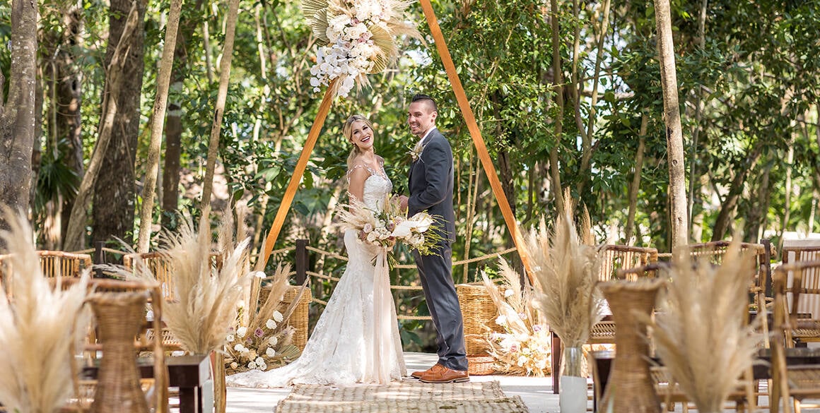 A bride and groom stand at a wooden altar in a tropical jungle