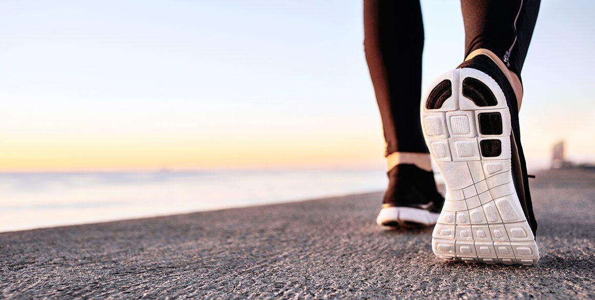 Close-up of a runner's sneakers with a beach at sunrise in the background.