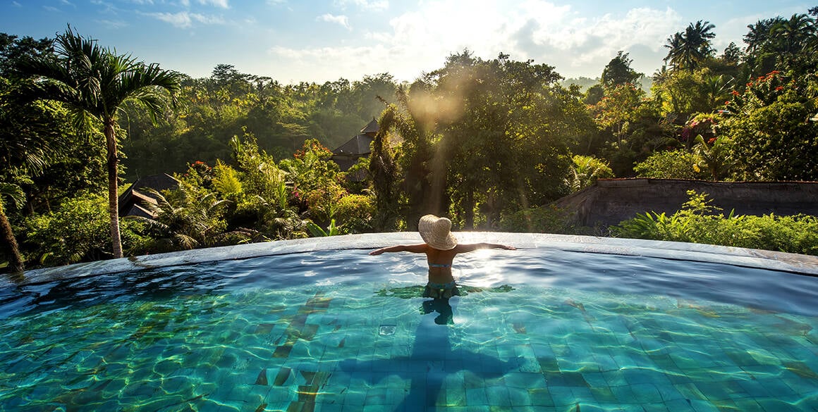 The back of a woman in an elevated infinity pool facing a jungle