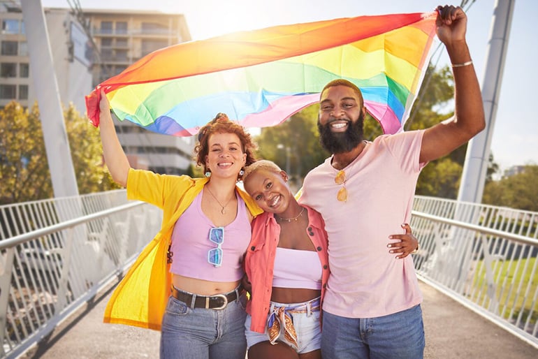 Three friends wearing pink shirts and holding a rainbow flag