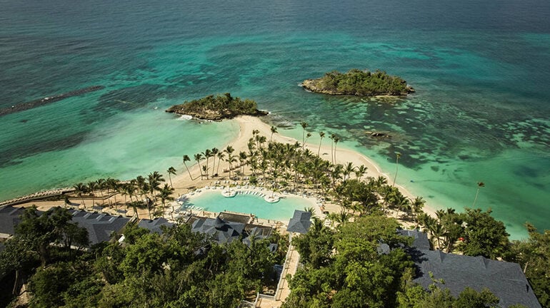 Overhead distance aerial view of a large resort pool on an island with two offshore islands in the Caribbean