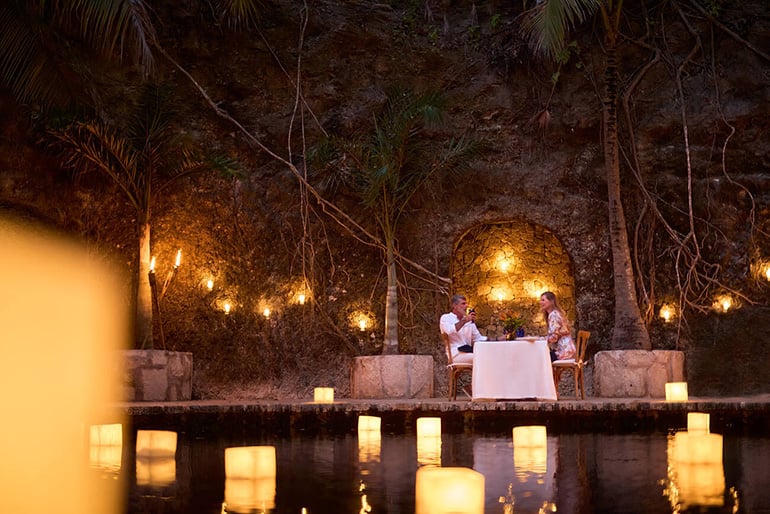 A couple having dinner by a cenote with candles all around them