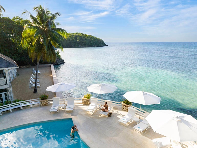 A woman on a lounge chair and man in a pool overlooking the ocean in Jamaica