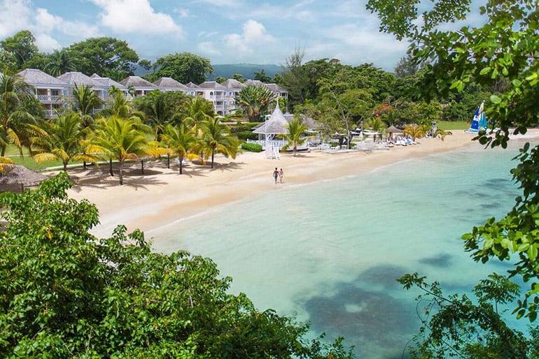 Far-out perspective of a couple walking along a beach at a Couples Sans Souci in Jamaica