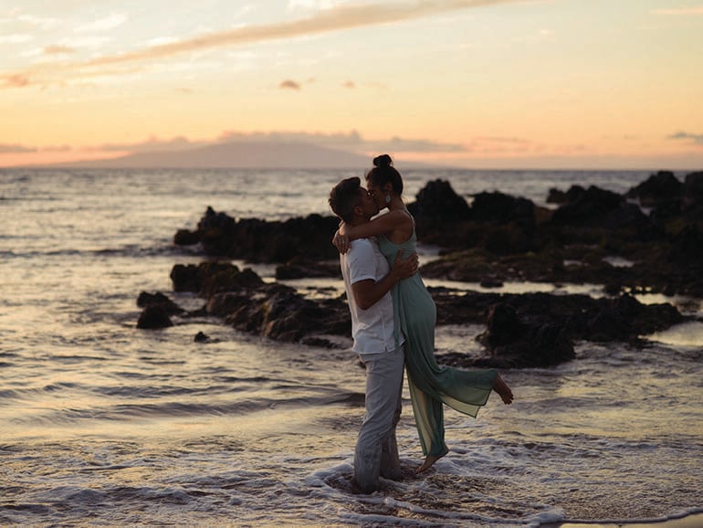 A man and woman kissing in the ocean at sunset