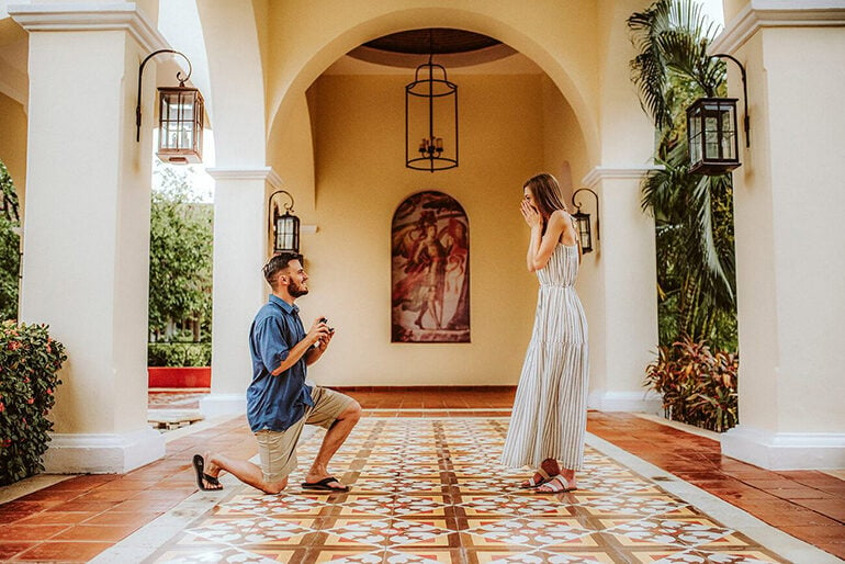 A man on bended knee with a woman in a white dress holding her face in her hands