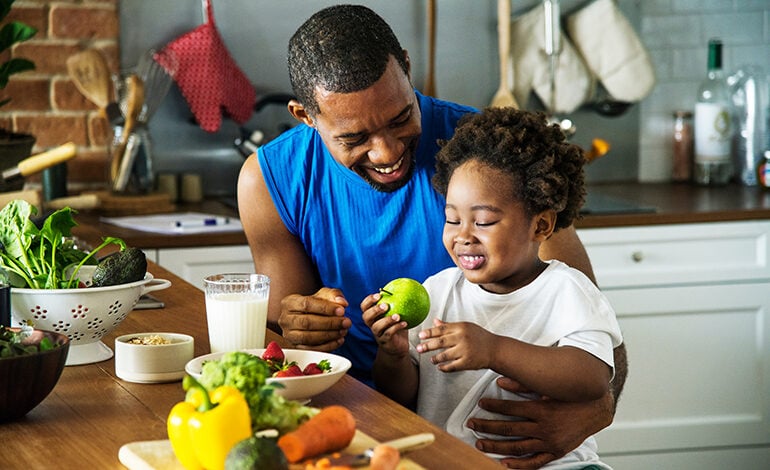 A father and his young son prepare to cook with fruits and vegetables