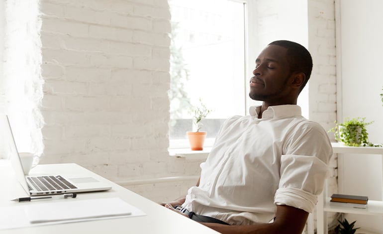 A man sits at his desk practicing deep breathing