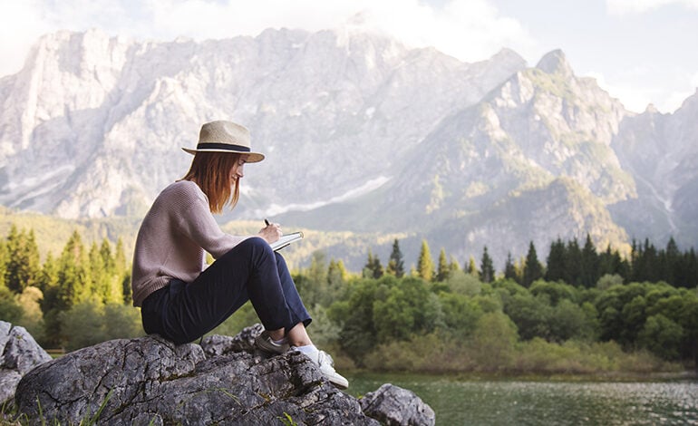 A woman writing in her journal with a mountain lake in the background