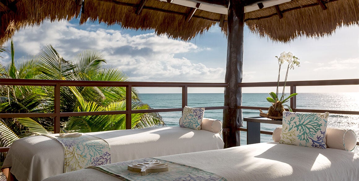 Two massage tables elevated in a palapa with ocean views